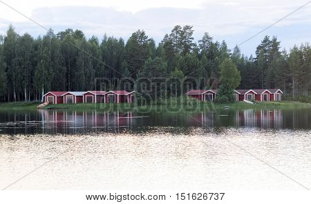 Group of red boathouse reflecting in the water birch trees in the background