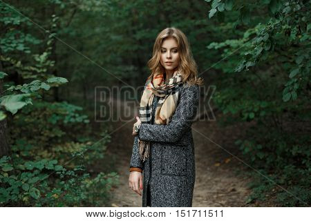Beautiful Young Woman In A Knitted Scarf And Autumn Coat Near The Green Leaves