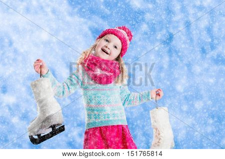 Happy laughing little girl having fun ice skating in snowy park. Winter sport and outdoor activity for family with children on Christmas vacation. Funny kid playing with snow. Child holding skates.