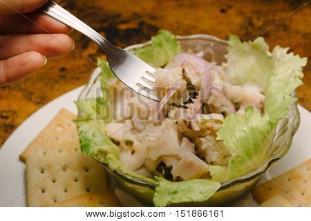 Ceviche with presentation, cookies around. Hand holding fork
