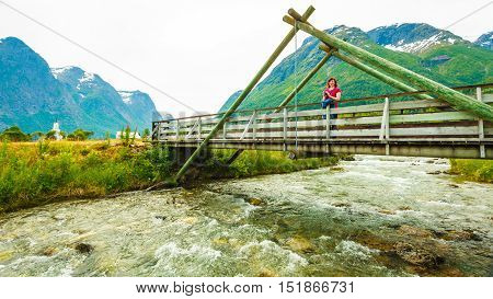 Tourism vacation and travel. Woman tourist relaxing on bridge looking at mountains landscape in norwegian village Oppstryn Sogn og Fjordane county. Norway Scandinavia.
