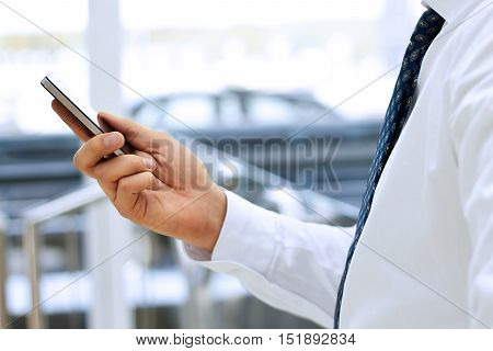 Cropped view of Businessman holding the mobile phone standing in front the window