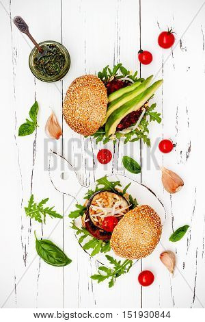 Fresh homemade two veggies burgers served on cutting board over white rustic table. Vegan grilled eggplant arugula sprouts and pesto sauce burger. Veggie beet and quinoa burger with avocado. Top view overhead flat lay