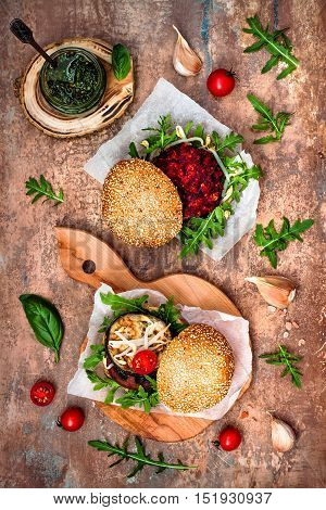 Fresh homemade two veggies burgers served on cutting board over stone vintage background. Vegan grilled eggplant arugula sprouts and pesto sauce burger. Veggie beet and quinoa burger. Top view overhead flat lay.