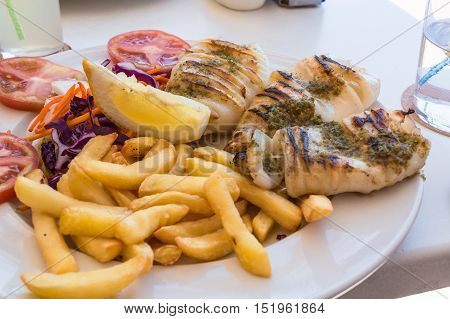 Grilled octopus. Grilled squid served with french fries and lemon and salad.