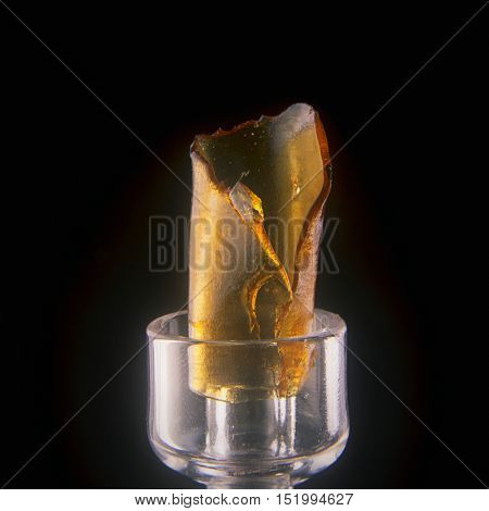 A piece of cannabis oil concentrate aka shatter with glass tools isolated against black background
