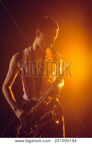 Handsome Young Jazzman Playing Saxophone Against Spotlight
