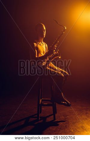 Young Jazzman Looking At Camera While Sitting On Stool And Holding Saxophone