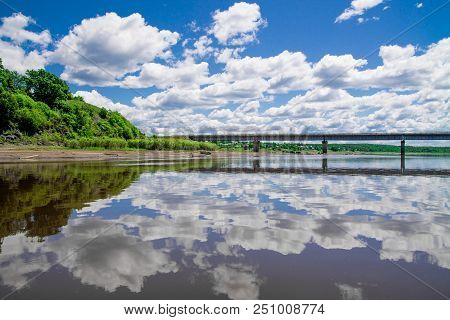 Steel Bridge With Lots Of Clouds In The Sky And Their Reflection In Water
