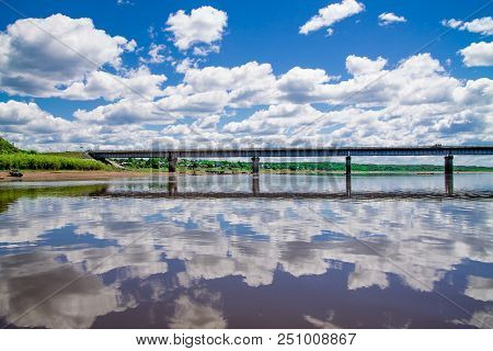 Steel Bridge With Lots Of Clouds In The Sky And Their Reflection In Water