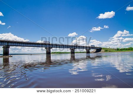 Steel Bridge With Lots Of Clouds In The Sky And Their Reflection In Water