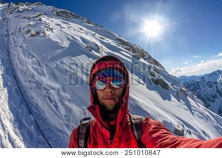 Selfi Male Mountaineer In Snowy Mountains, Wearing A Helmet With A Backpack.
