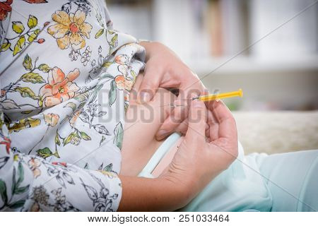 Woman is doing an insulin or heparin injection in her abdomen at home