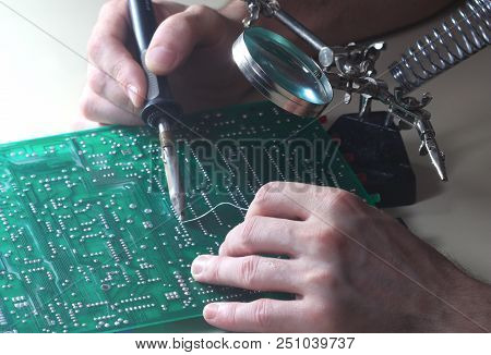 Tehnician Repair Circuit Board With Soldering Iron And Magnifying Glass In Laboratory
