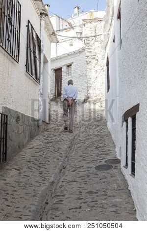 Elderly Local Man Slowly Climbing Sloped Street Of Alpujarras Town. Pampaneira, Granada, Spain