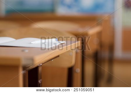 Notebook And Pen Are On The Table. School Classroom In Blur Background Without Young Student.