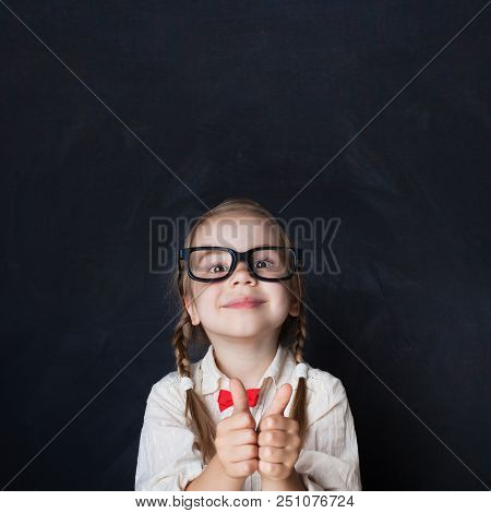 Сurious Girl In Glasses Showing Hands With Thumb Up And Smiling On Chalk Board Background. Child Thu