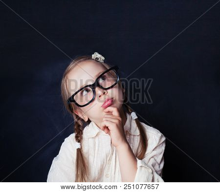 Сurious Little Girl Thinking On Empty Chalk Board Background With Copy Space. Child Back To School, 