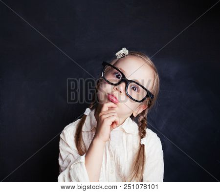 Сurious Child Thinking. Funny Little Girl In Glasses On Chalk Board Background With Copy Space. Back