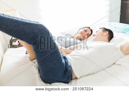 Multiethnic Lovers With Feet Up Smiling While Lying On Bed At Home