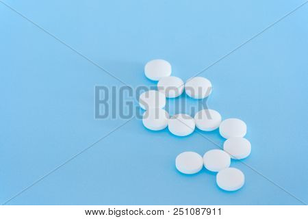 White Pills Spilling Forming A Dollar Sign On A Blue Background.