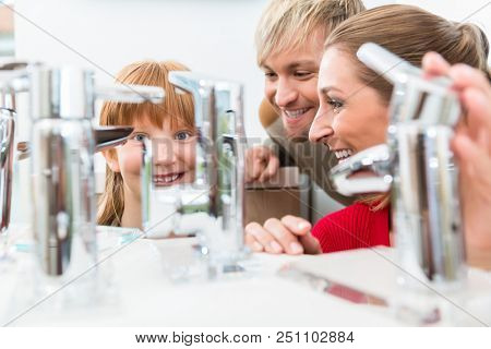 Low-angle portrait of a happy family, looking for a new bathroom sink faucet in a modern sanitary ware shop with high-quality fixtures and appliances