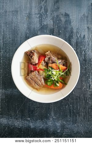 Sturdy Shurpa, Chorba or Shorba Soup with Mutton and Vegetables Top View. Clear Homemade Halal Broth with Large Pieces of Lamb, Carrots, Potatoes, Bell Peppers, Onions, Parsley