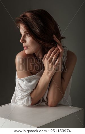 A Beautiful Brunette Girl With Her Hair Spread On One Side Stands Leaning On A White Table And Strai