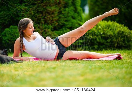Pregnant Woman Performing Side Reclining Leg Lift While Lying On Yoga Mat In Park