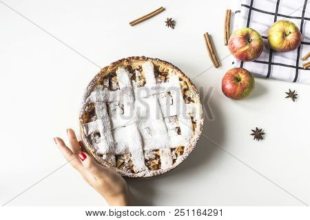 Homemade apple pie sprinkled with powdered sugar in female hand on a white table next to apples, cin