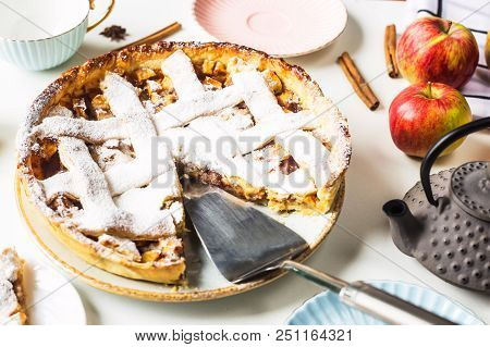 Homemade Apple Pie Sprinkled With Powdered Sugar In Female Hand On A White Table Next To Apples, Cin