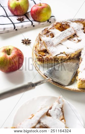 Homemade Apple Pie Sprinkled With Powdered Sugar In Female Hand On A White Table Next To Apples, Cin