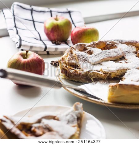 Homemade Apple Pie Sprinkled With Powdered Sugar In Female Hand On A White Table Next To Apples, Cin
