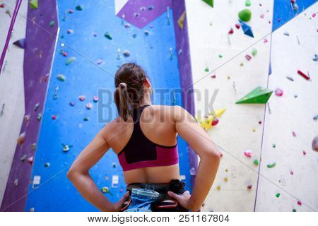 Photo of young athlete girl from back with hands on waist-standing next to wall for rock climbing