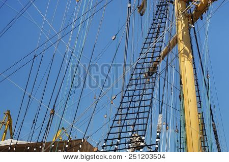 Masts Of A Sailing Ship With The Lowered Sails With Blue Sky On The Background.