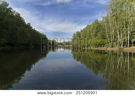The Shores Are Reflected In The Surface Of The Pond. Forest Park Troparevo, Moscow, Russia. Sunny Da