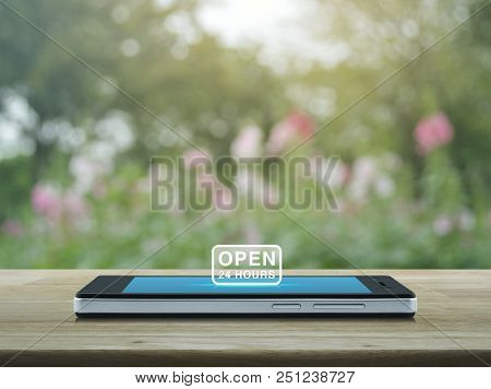 Open 24 Hours Icon On Modern Smart Phone Screen On Wooden Table Over Blur Pink Flower And Tree, Busi