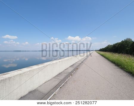 Walkway With Lamps On Barrage At Countryside Landscapes Of Lake, Grassy Field, Forest On European Ar