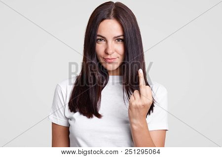 Bad Girl With Straight Dark Hair Shows Fuck Sign, Looks Mysteriously At Camera, Wears Casual T Shirt