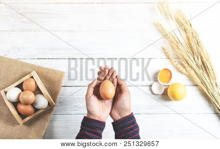 Hands Holding Brown Egg On White Wood Background