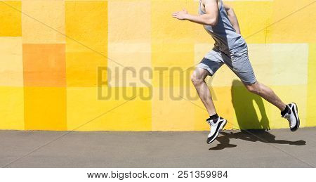Unrecognizable Athlete Man Running Against Bright Yellow Graffiti Wall, Copy Space, Crop