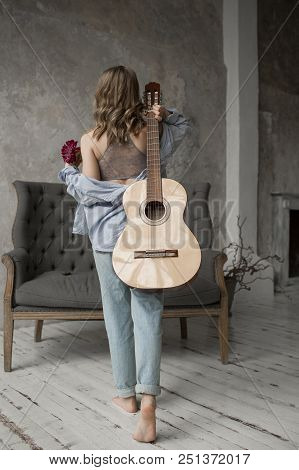 Blonde Curly Girl Holding Yellow Acoustic Guitar And Go To The Grey Sofa. Blonde Curly Girl Holding 