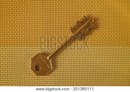 Golden Key On Two Toned Woven Yellow Textile. Conceptual Key As Symbol For Acces, Property Or Securi