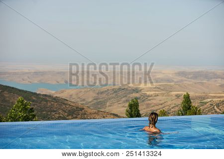 Young Woman Relaxaing In The Swimming Pool Looking At The Nature Landscape View On Background. Trave
