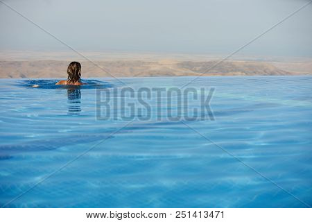 Young Woman Relaxaing In The Swimming Pool Looking At The Nature Landscape View On Background. Trave