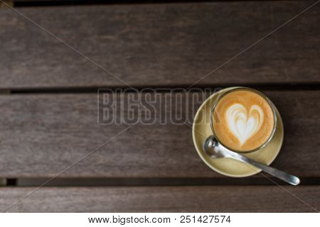 A Glass Cup Of Cappuccino With Heart Shape Latte Art, Sauser And Tea Spoon On The Wooden Table. Flat