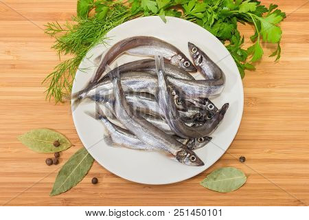 Top View Of The White Dish With Defrosted Uncooked Capelin, Bay Leaf, Allspice And Fresh Parsley And