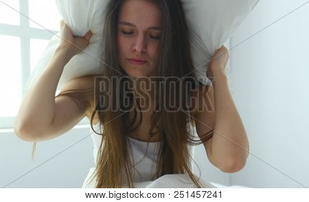 Young caucasian woman covering her head and ears with pillows.