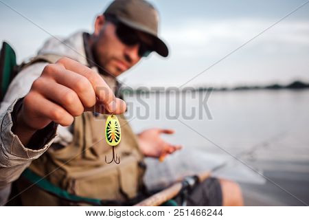Man Is Showing Artificial Silicon Baits On Camera. He Is Looking At It As Well. Man Is Sitting At Th