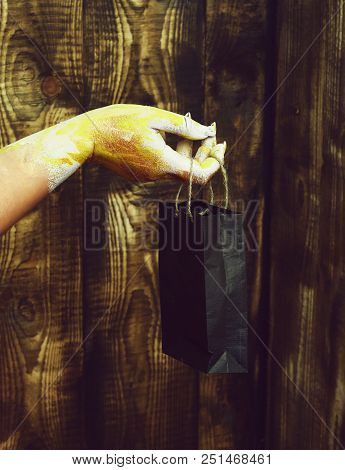 Female Hand Smeared In Golden Paint Or Glister Holding Black Package Or Bag On Brown Vintage Studio 